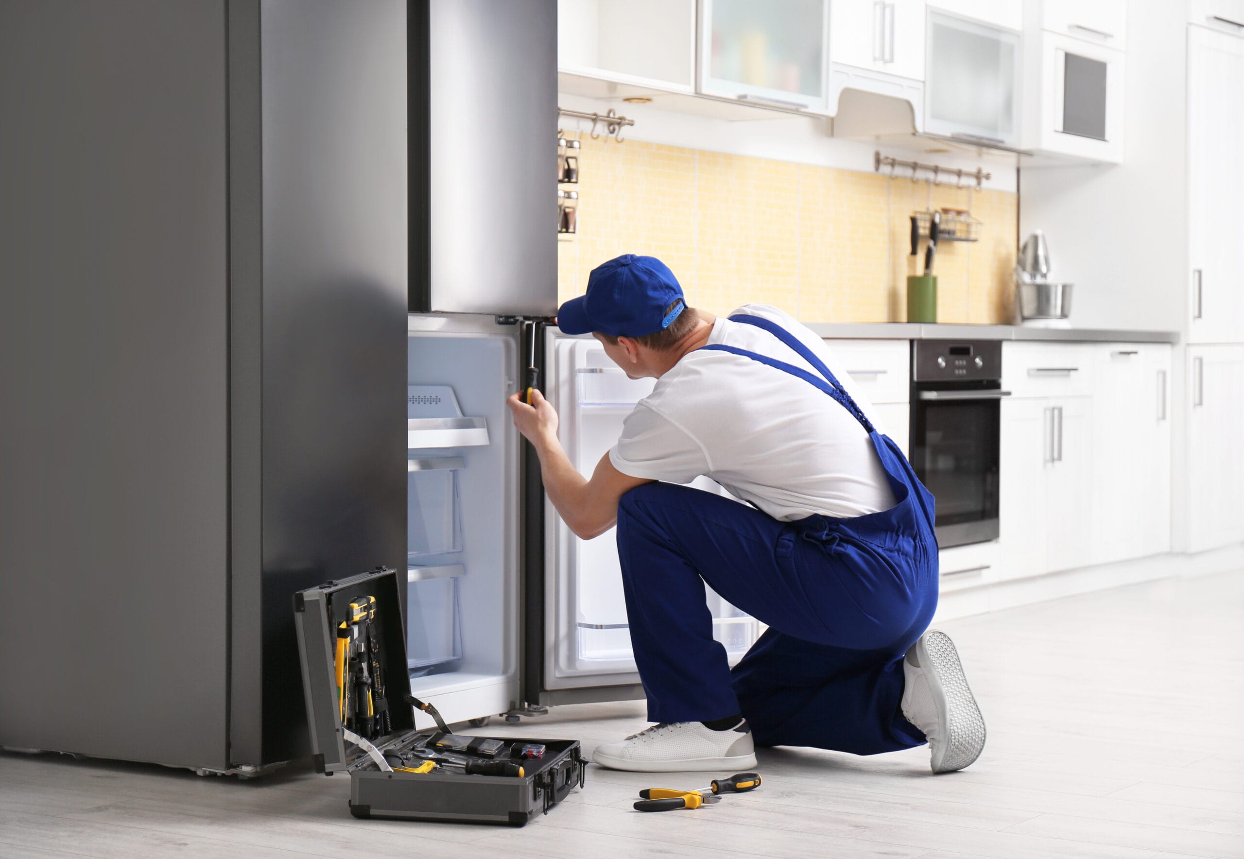 Male technician with screwdriver repairing refrigerator in kitch Plumbers Winnipeg